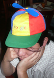 Asian man in his twenties wearing a blue, green, yellow and red propellor hat that says